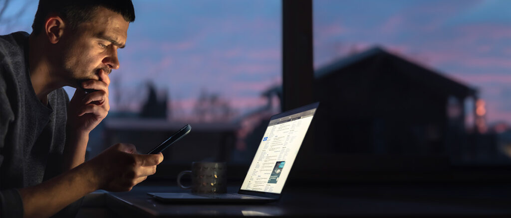 Man arbetar sent på kvällen med laptop och telefon i mörkret – illustrerar UC Berkeley-studiens fynd att AI intensifierar arbetet och leder till längre arbetsdagar och utbrändhet